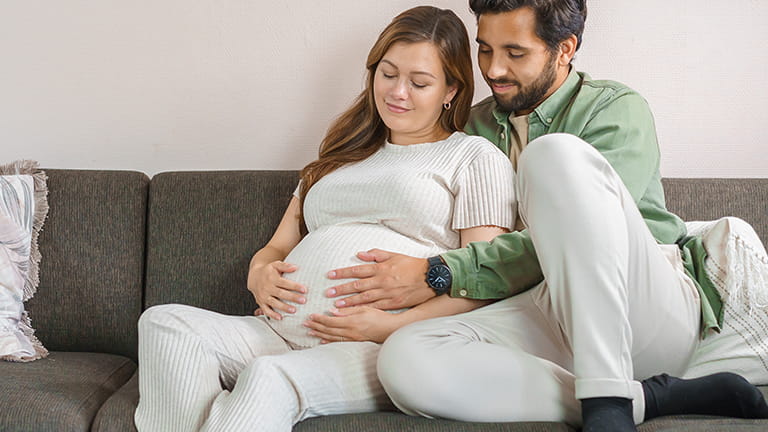 Man en vrouw op de bank waarbij de man de zwangere buik knuffelt