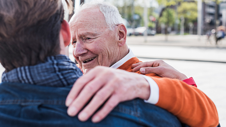 Oudere man legt hand op de schouder van mantelzorger