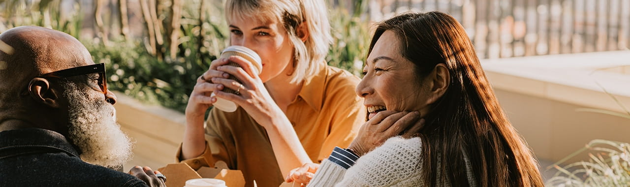 Man en twee vrouwen drinken buiten koffie en lachen samen