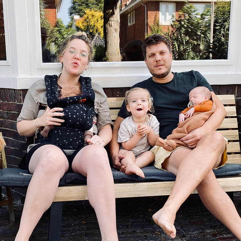 Gezin met tweeling, dochter en hond voor het huis op het bankje