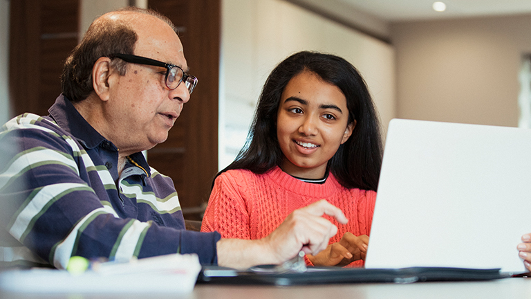 Young woman explains something to an older man on computer