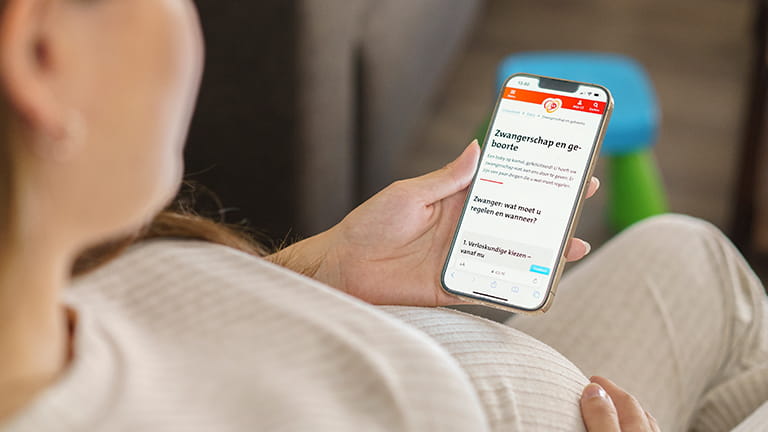 Vrouw op bank scrolt op telefoon door webpagina's van CZ over zwangerschap