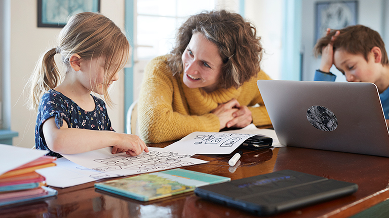 Moeder met twee jonge kinderen aan de eettafel met laptop en kindertekening