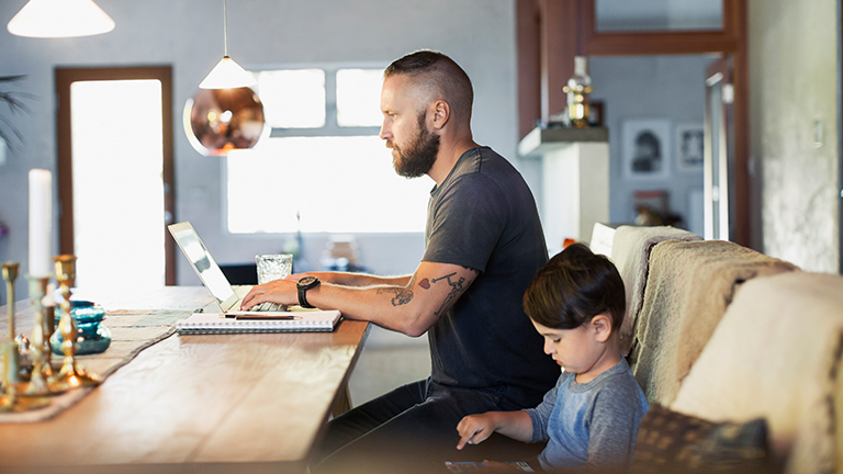 Man zit achter laptop aan keukentafel en zoontje zit ernaast